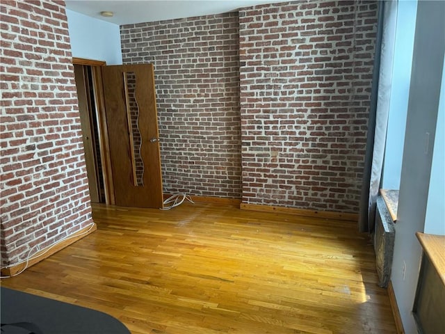 unfurnished room with hardwood / wood-style floors and brick wall