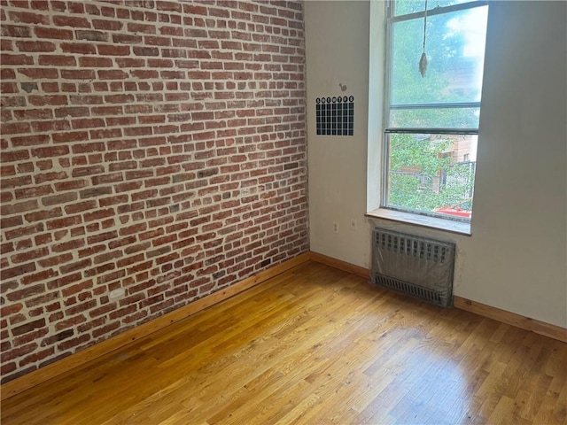 empty room with light wood-type flooring, radiator, and brick wall