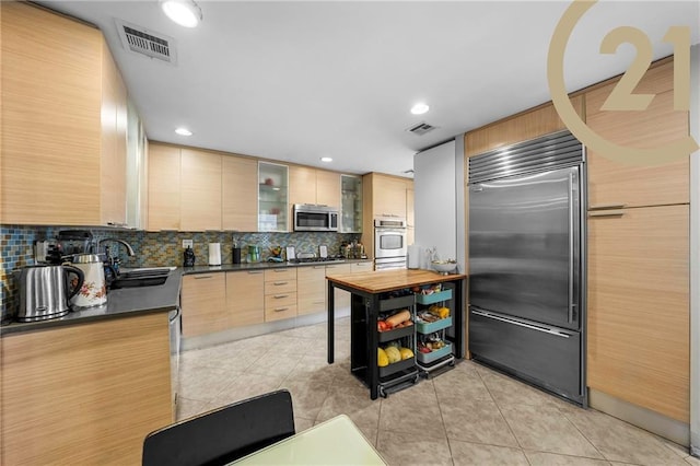 kitchen featuring tasteful backsplash, stainless steel appliances, light brown cabinets, light tile patterned floors, and sink