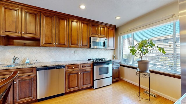 kitchen featuring stainless steel appliances, light hardwood / wood-style flooring, sink, backsplash, and light stone counters