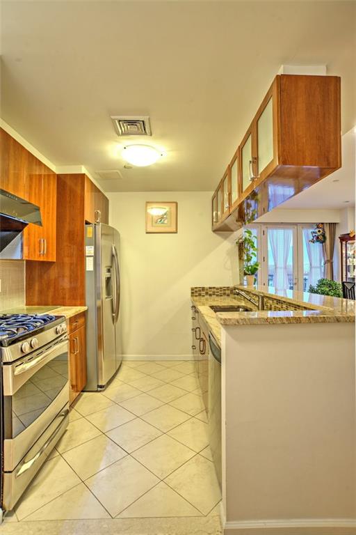 1740 W 4th St Unit 4C, Brooklyn, NY 11223 - kitchen with appliances with stainless steel finishes, light stone counters, glass insert cabinets, brown cabinets, and light tile patterned floors