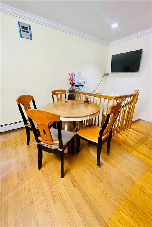 dining space with a baseboard radiator, ornamental molding, and wood-type flooring