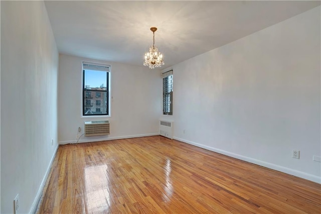 empty room featuring a wall unit AC, light wood finished floors, radiator, an inviting chandelier, and baseboards