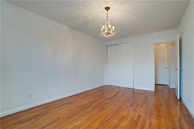 unfurnished bedroom with light wood-style floors, a closet, baseboards, and an inviting chandelier