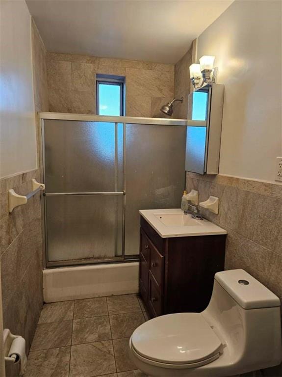 bathroom with toilet, shower / bath combination with glass door, tile walls, and vanity