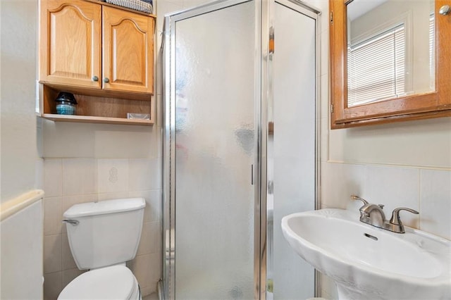 bathroom featuring toilet, a stall shower, a sink, and tile walls