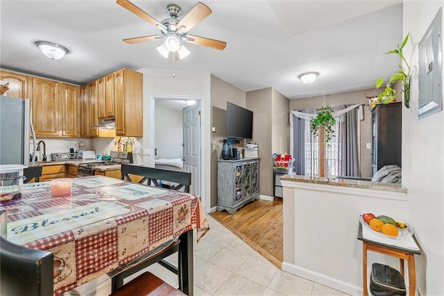 kitchen with light tile patterned floors, appliances with stainless steel finishes, a peninsula, under cabinet range hood, and a sink