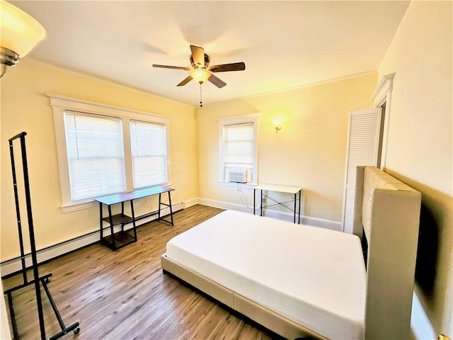 bedroom with a baseboard heating unit, ceiling fan, baseboards, and wood finished floors