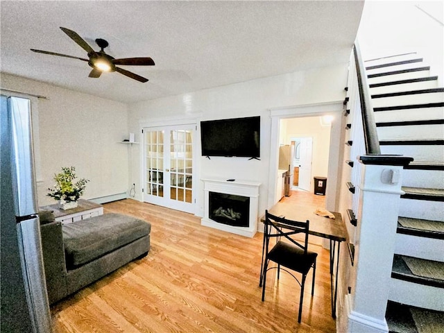 living room with ceiling fan, a textured ceiling, a fireplace, wood finished floors, and baseboard heating