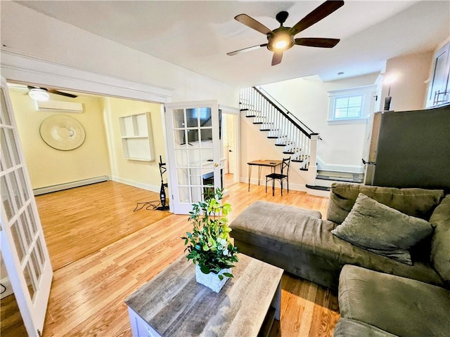 living room with stairway, a baseboard radiator, a ceiling fan, and light wood-style floors