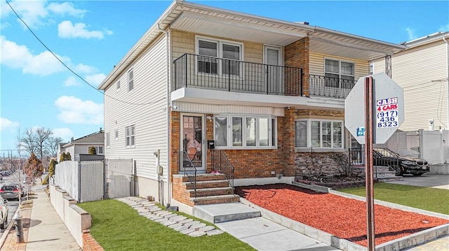 view of front of property featuring a balcony, a front yard, fence, and brick siding