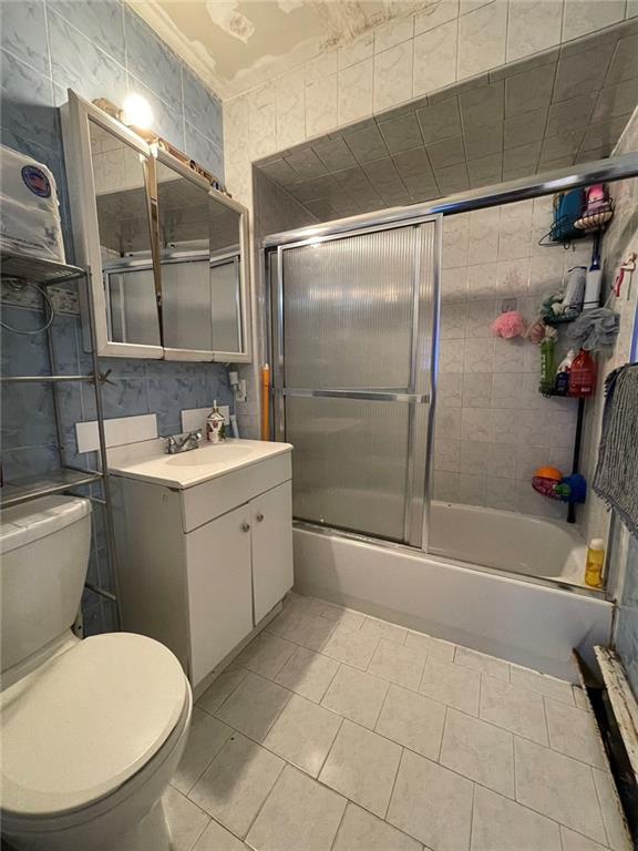 bathroom with toilet, combined bath / shower with glass door, vanity, and tile patterned floors