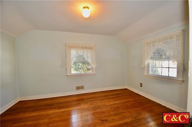 spare room with vaulted ceiling, dark wood-style floors, visible vents, and a healthy amount of sunlight