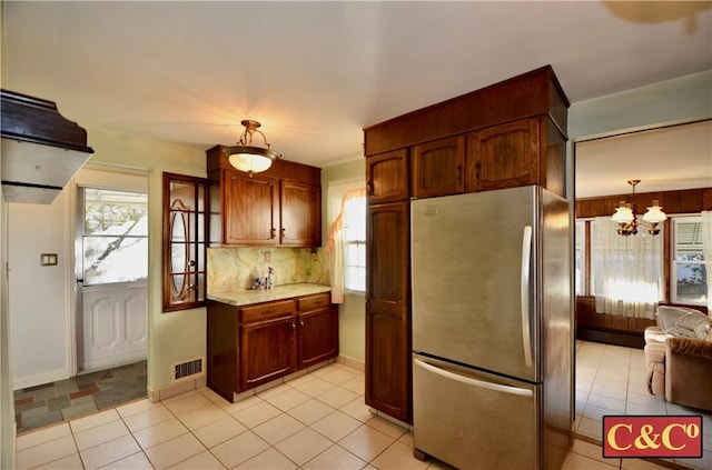 kitchen featuring light tile patterned floors, light countertops, hanging light fixtures, freestanding refrigerator, and tasteful backsplash