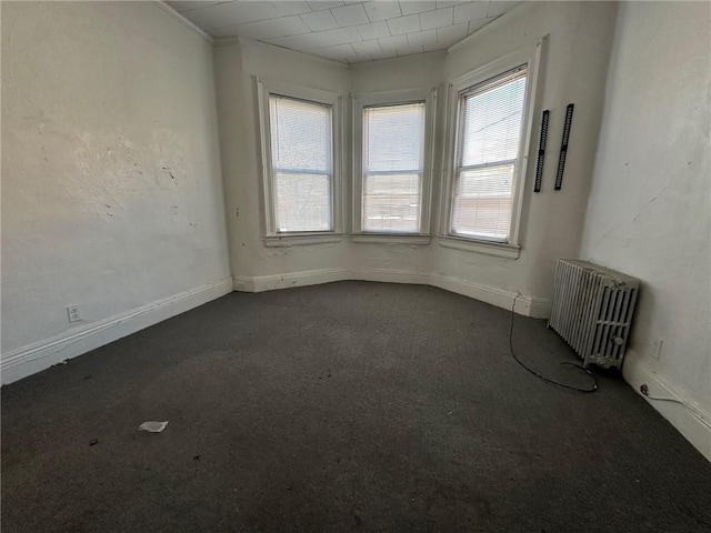 unfurnished room with baseboards, dark colored carpet, and radiator