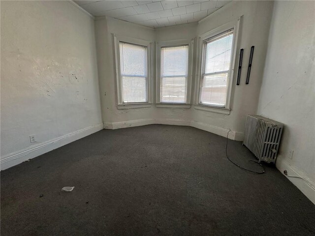 spare room featuring dark colored carpet, radiator heating unit, crown molding, and baseboards