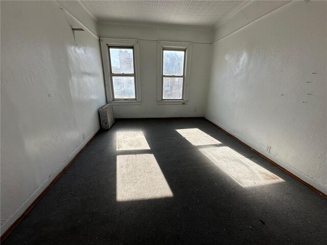 spare room featuring carpet floors, a textured wall, baseboards, and radiator