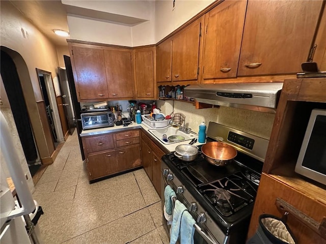 kitchen with stainless steel appliances, arched walkways, a toaster, ventilation hood, and brown cabinetry