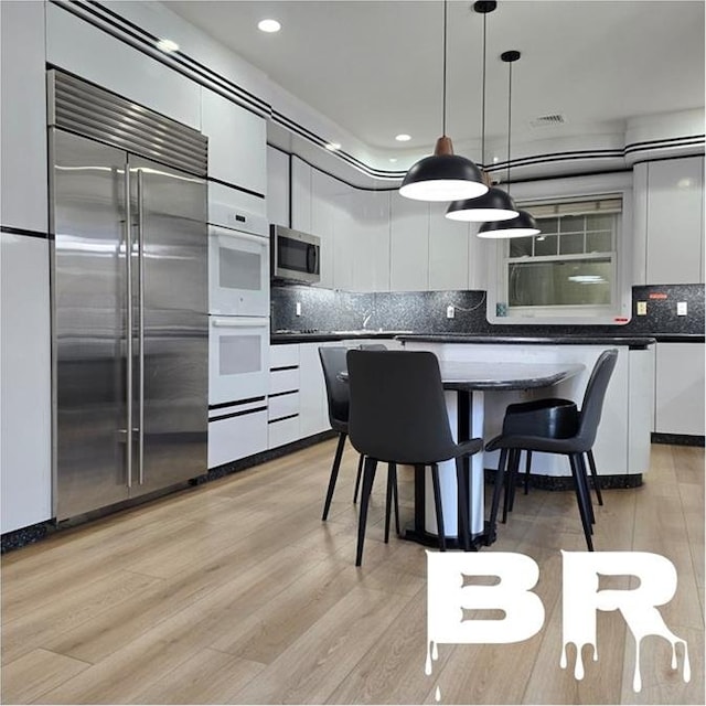 kitchen featuring dark countertops, white cabinetry, appliances with stainless steel finishes, and hanging light fixtures