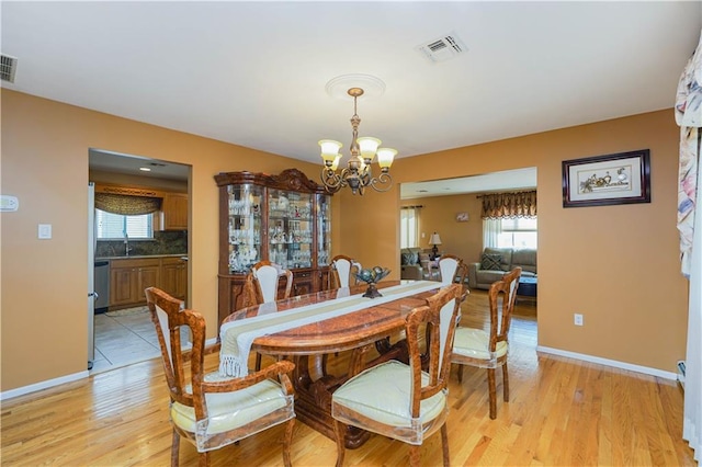 dining space featuring light wood-style floors, visible vents, baseboards, and an inviting chandelier