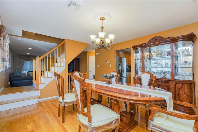 dining area featuring light wood-style flooring, visible vents, a notable chandelier, and stairway