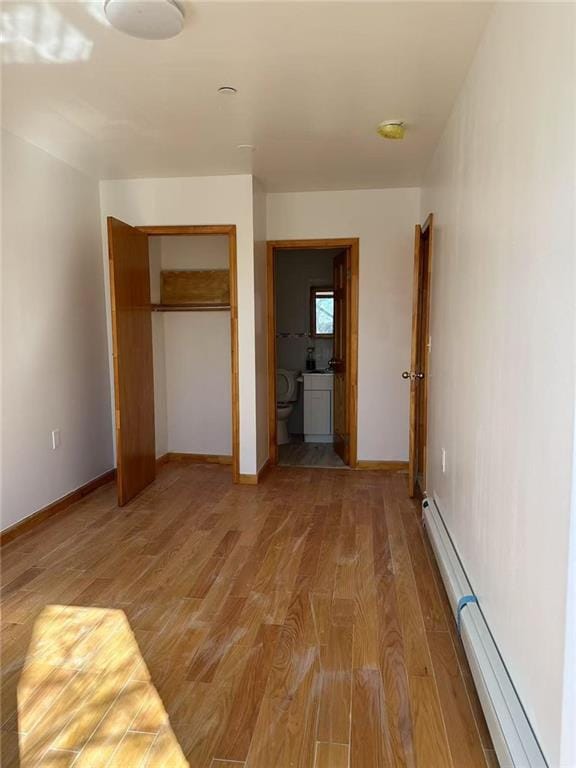 unfurnished bedroom with baseboards, light wood-style flooring, a baseboard heating unit, and a closet