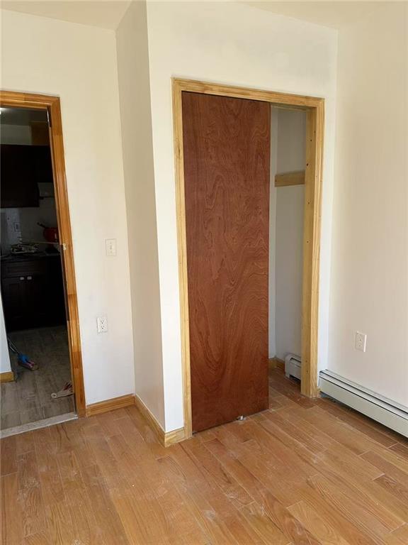 unfurnished bedroom with a baseboard heating unit, a closet, light wood-style flooring, and baseboards