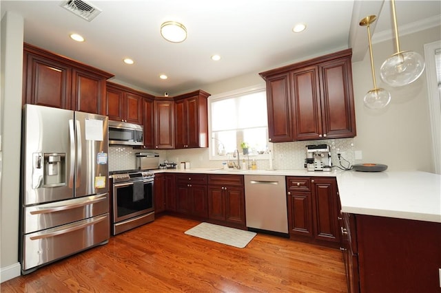 kitchen with tasteful backsplash, dark wood finished floors, appliances with stainless steel finishes, hanging light fixtures, and light countertops