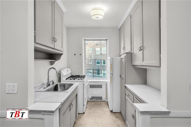 kitchen with radiator heating unit, light countertops, white appliances, light tile patterned floors, and a sink