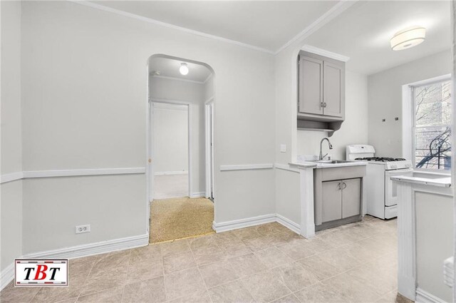 kitchen featuring arched walkways, light countertops, gray cabinetry, a sink, and white gas range oven