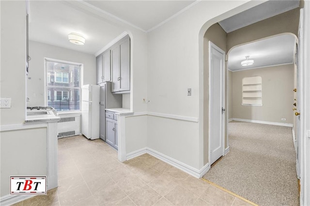 kitchen featuring radiator, light countertops, arched walkways, freestanding refrigerator, and crown molding