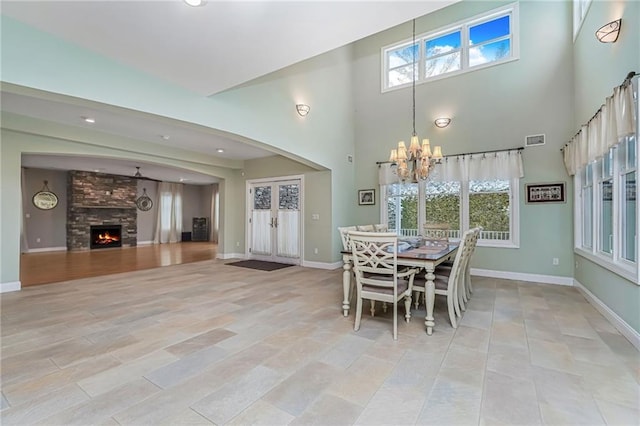 dining space featuring a large fireplace, visible vents, baseboards, an inviting chandelier, and a wealth of natural light