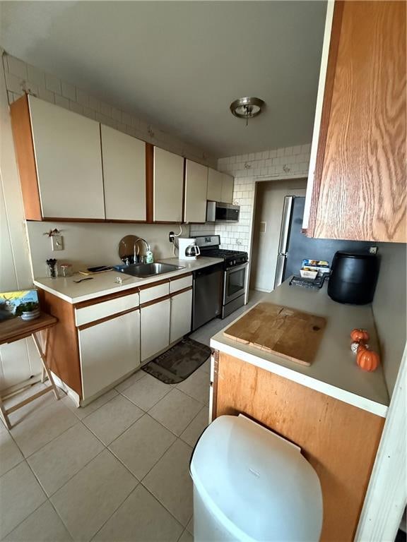 kitchen with a sink, stainless steel appliances, light countertops, light tile patterned floors, and decorative backsplash