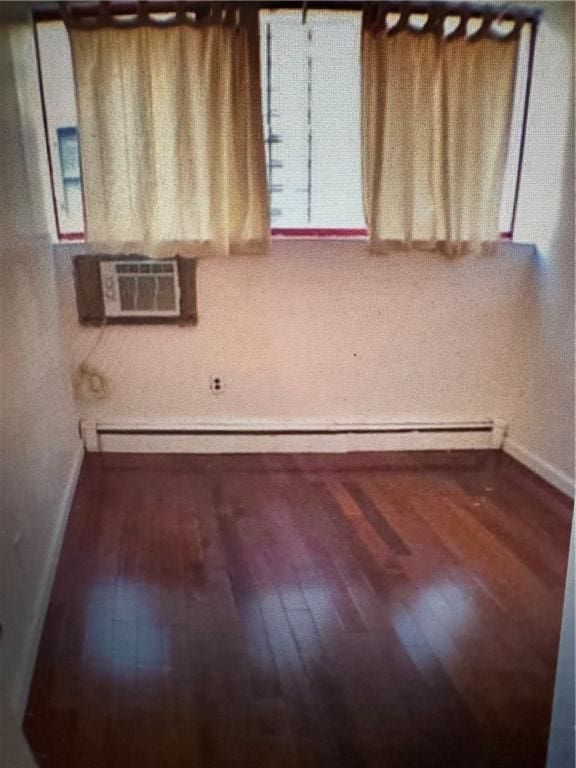 empty room with baseboard heating, a wall unit AC, dark wood finished floors, and baseboards