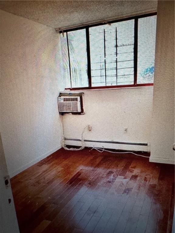 unfurnished room with a baseboard heating unit, an AC wall unit, and wood finished floors