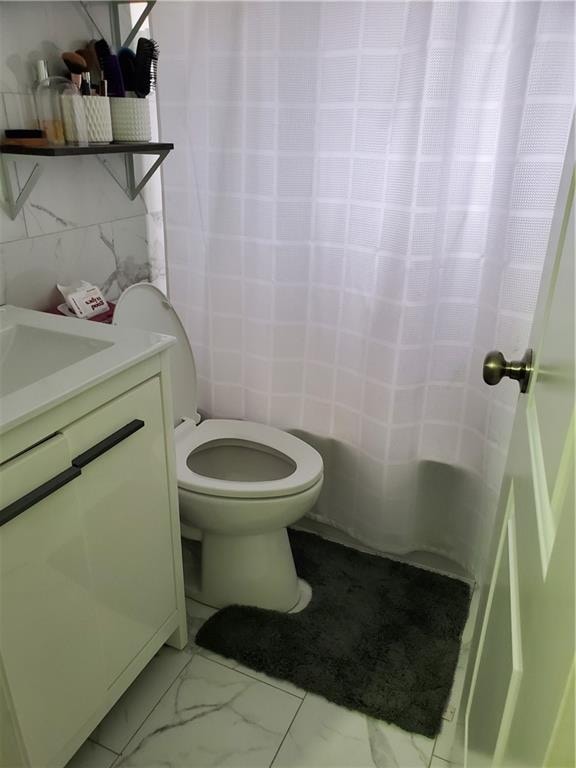 bathroom featuring marble finish floor, tile walls, toilet, vanity, and a shower with curtain