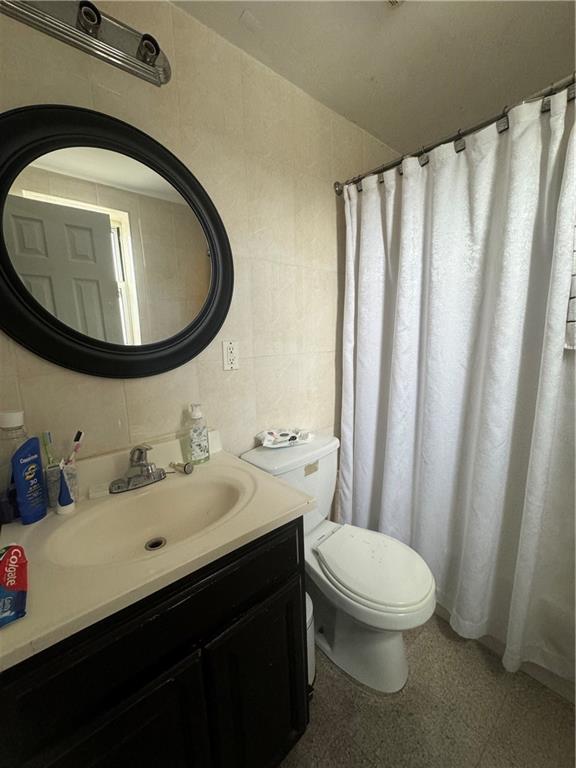 bathroom with toilet, vanity, and tile walls