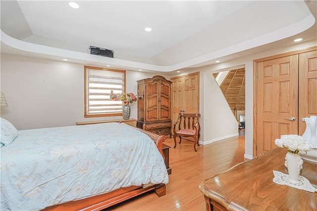 bedroom featuring recessed lighting, a raised ceiling, light wood-style flooring, and baseboards