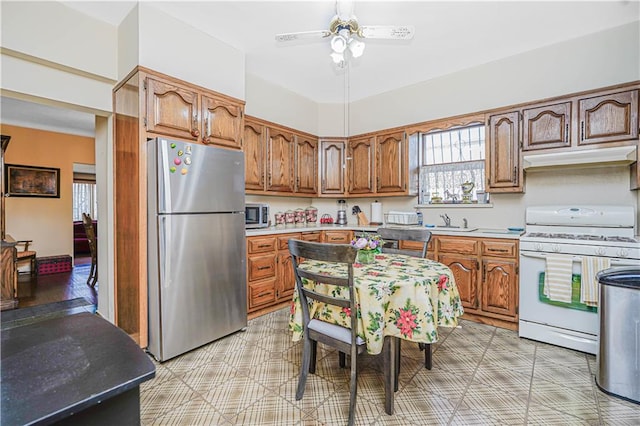 1265 86th St, Brooklyn, NY 11228 - kitchen featuring appliances with stainless steel finishes, a ceiling fan, light countertops, under cabinet range hood, and brown cabinets