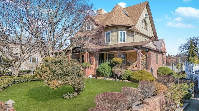 victorian home featuring a porch, brick siding, fence, a front lawn, and a chimney