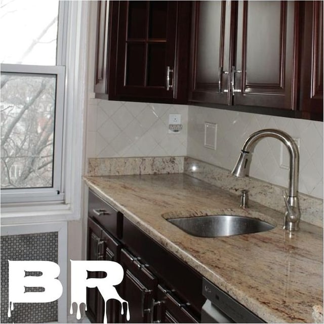 kitchen featuring light stone countertops, a sink, decorative backsplash, and dark brown cabinets