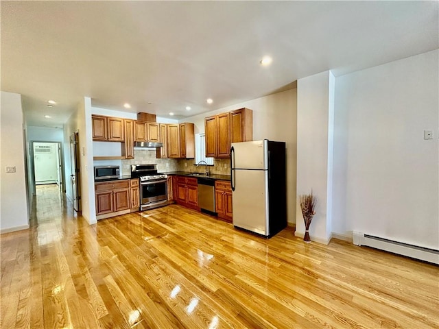 kitchen featuring a sink, light wood-style floors, under cabinet range hood, appliances with stainless steel finishes, and dark countertops