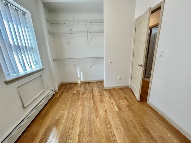 laundry area with light wood finished floors, baseboard heating, and baseboards