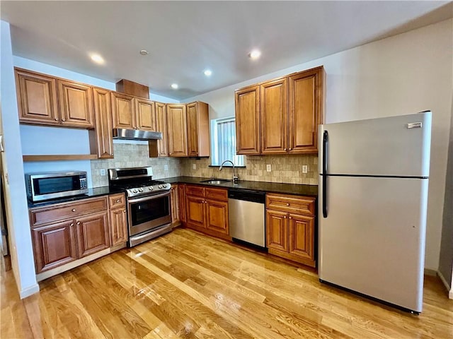 kitchen featuring decorative backsplash, stainless steel appliances, light wood-type flooring, under cabinet range hood, and a sink