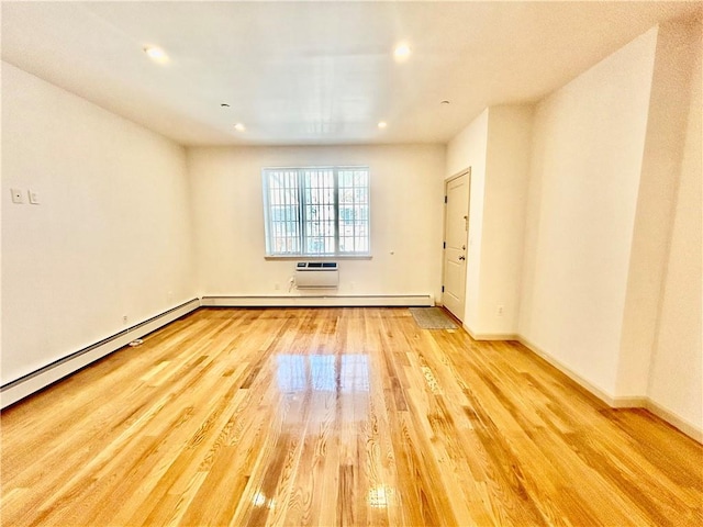 empty room with a wall mounted AC, a baseboard radiator, light wood-style flooring, and baseboards