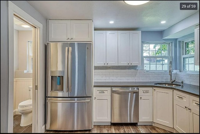 kitchen with stainless steel appliances, dark countertops, a sink, and white cabinetry