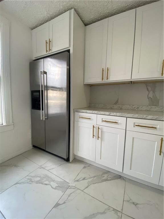 kitchen featuring a textured ceiling, high quality fridge, marble finish floor, and white cabinetry