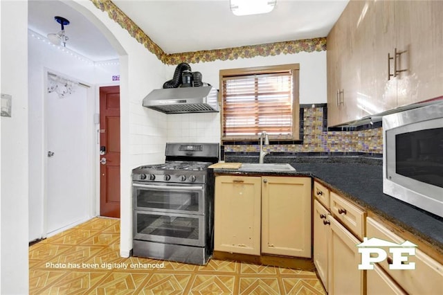 kitchen featuring decorative backsplash, dark countertops, appliances with stainless steel finishes, wall chimney range hood, and a sink