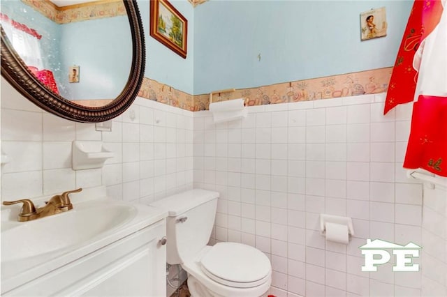 half bath with wainscoting, tile walls, toilet, and vanity