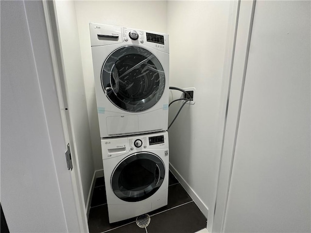 clothes washing area featuring laundry area, stacked washer / dryer, tile patterned flooring, and baseboards